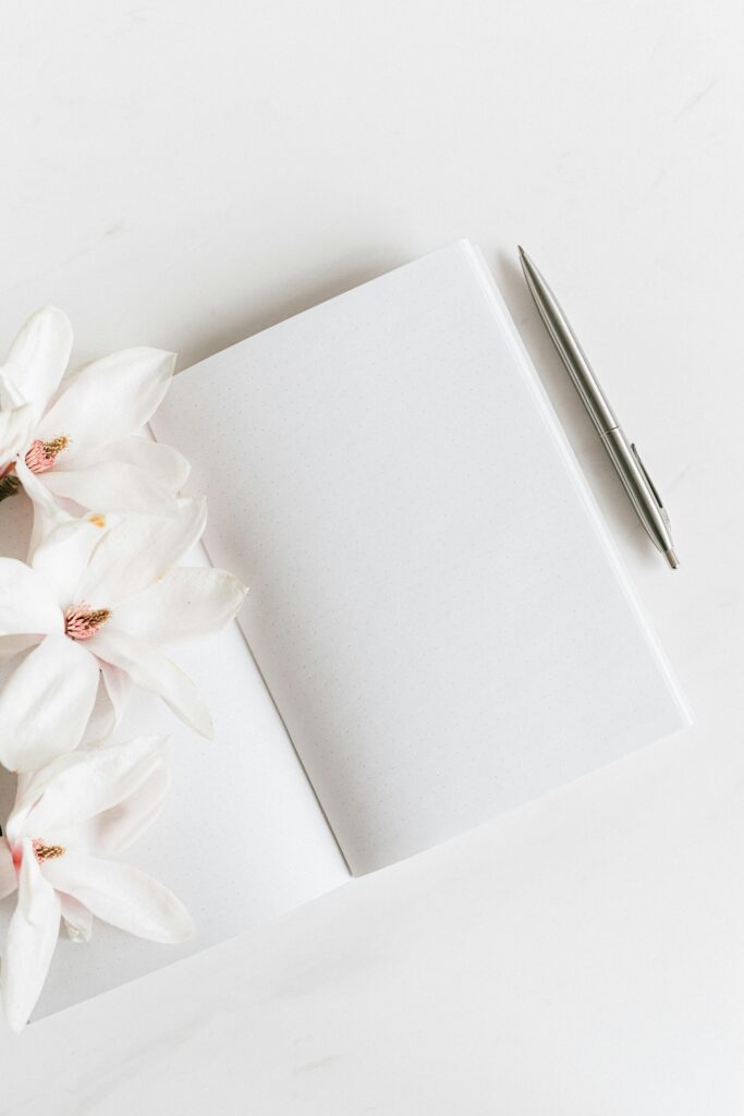 Top view of a blank notebook with magnolias and a silver pen, ideal for notes or journaling.